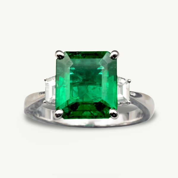 Emerald three-stone ring in 18K white gold with a 2.98-carat Colombian emerald and trapeze-cut diamonds.