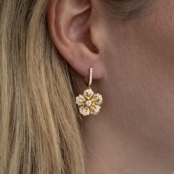diamond-floral-earrings-on-ear.jpg Diamond floral earrings in 18K yellow gold with softly curved petals, a central diamond, and diamond-set hoops by Claris-A.