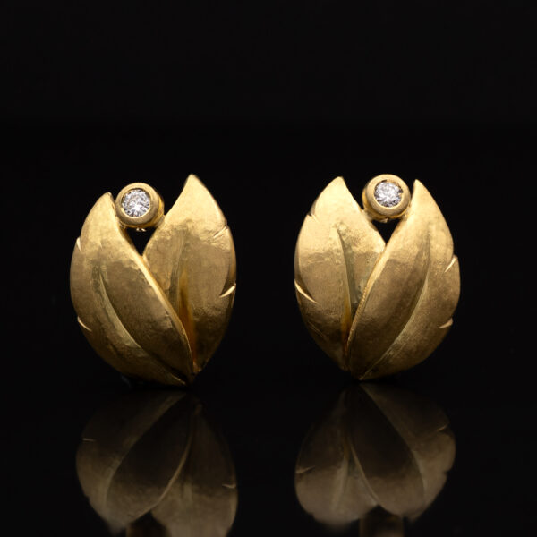 Hammered yellow gold leaf earrings with an open tip design, each set with a single diamond suspended between the curved terminals.