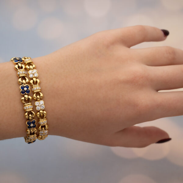 Articulated 18K yellow gold bracelet with rounded links and raised floral motifs set with sapphires and diamonds in a fluid design.