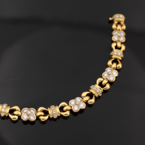Articulated 18K yellow gold bracelet with rounded links and raised floral motifs set with diamonds, forming a fluid, polished design.