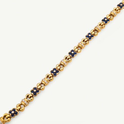 Cover_Website_BraceletClarisA_Sapphire Articulated 18K yellow gold bracelet with rounded links and raised floral motifs set with sapphires and diamonds in a fluid design.
