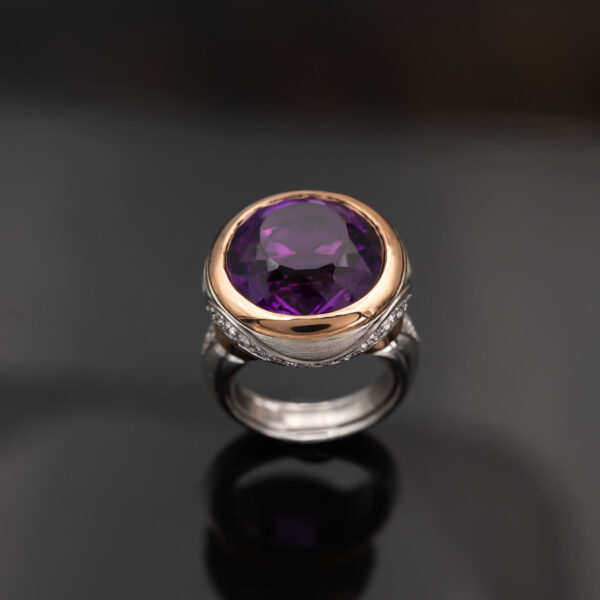 Claris-A-amethyst-diamond-cocktail-ring-white-yellow-gold-front 18K white and yellow gold cocktail ring with a large round purple amethyst in a yellow gold bezel, diamonds set along the gallery and shoulders, front view