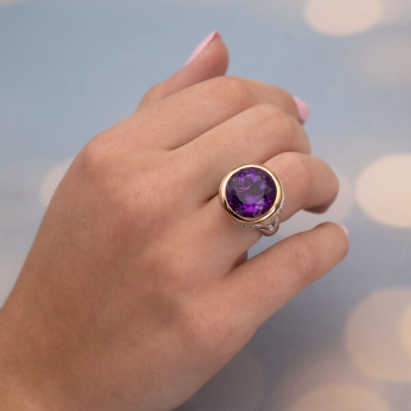 Claris-A-amethyst-diamond-cocktail-ring-white-yellow-gold-front 18K white and yellow gold cocktail ring with a large round purple amethyst in a yellow gold bezel, diamonds set along the gallery and shoulders, front view