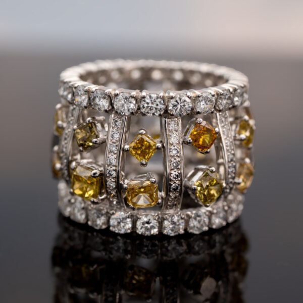 Wide 18K white gold ring with structured diamond-set bars and rows of white and fancy colored diamonds around the band