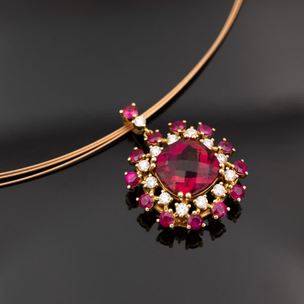 Close-up of a 18K rose gold pendant necklace featuring a central rubellite surrounded by rubies and diamonds in a floral cluster design