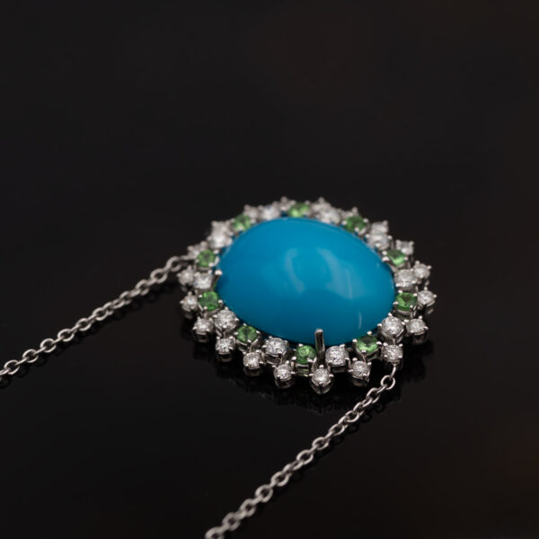 White gold pendant necklace with oval turquoise centre surrounded by tsavorites and diamonds in a floral sunburst motif.