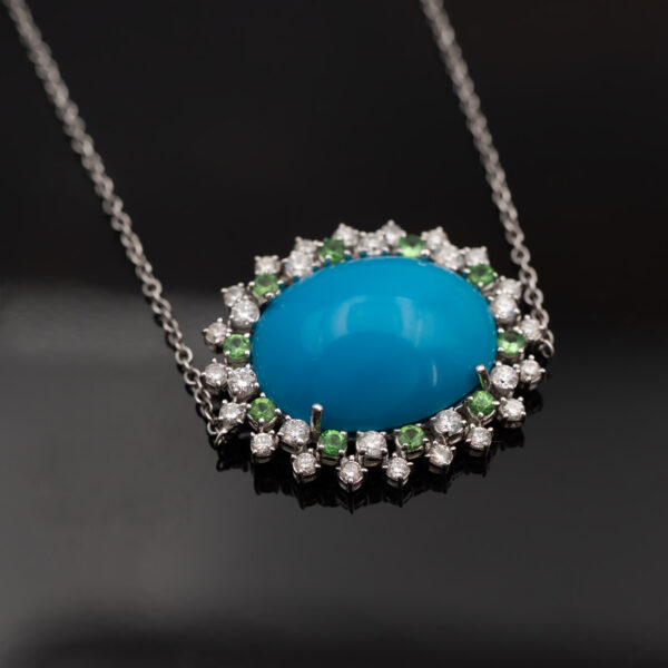 White gold pendant necklace with oval turquoise centre surrounded by tsavorites and diamonds in a floral sunburst motif.