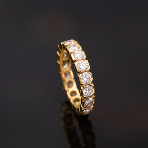 18K yellow gold eternity ring with round brilliant-cut diamonds in hexagonal gold settings.